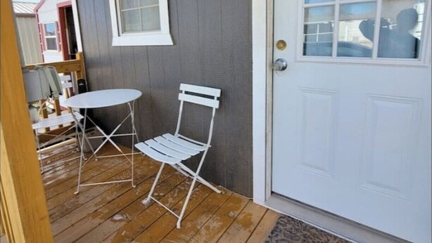 Una terraza de madera con una puerta blanca y una ventana.