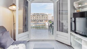 Un petit salon avec un canapé, un téléviseur et une vue sur un immeuble, visible à travers une porte vitrée.
