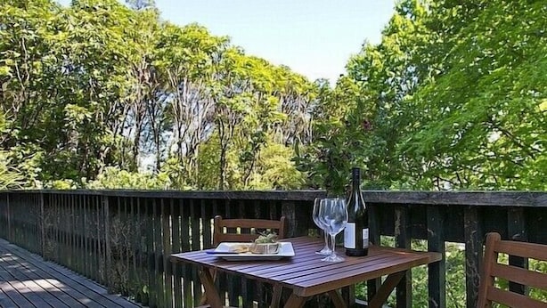 Eine Holzterrasse mit Tisch, Stühlen, einer Weinflasche und einem Glas.