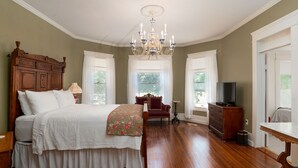 A bedroom with a wooden bed, a chandelier, a dresser, and a television. - Oaklea Mansion Bed and Breakfast (Winnsboro)