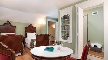 A bedroom with a bed, two chairs, a round table with a book and a teapot, and a wardrobe with shelves.