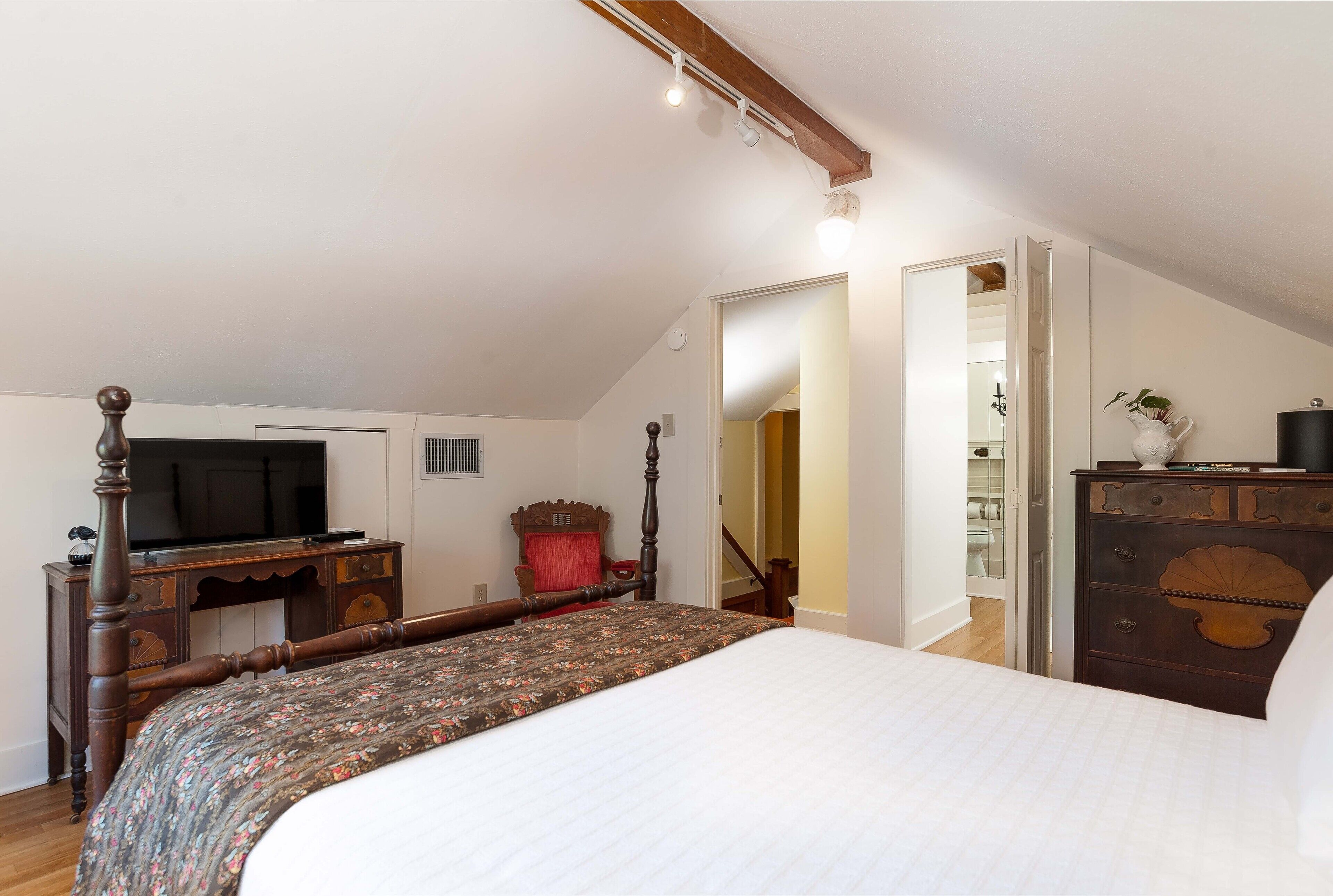 A bedroom with a large bed, a wooden dresser, a television, and a staircase leading to another room.