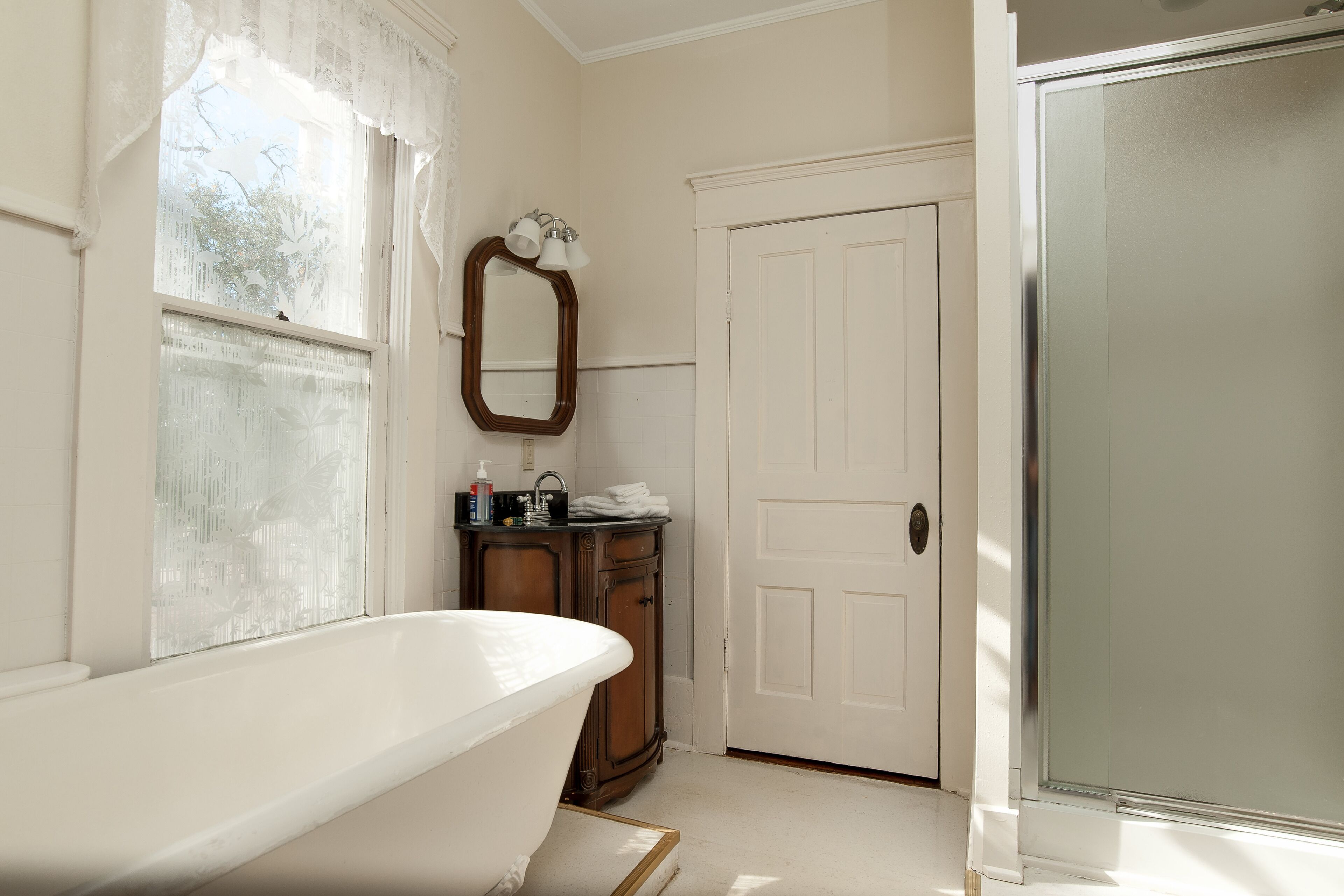 A bathroom with a freestanding bathtub, a wooden cabinet, a mirror, and a white door.