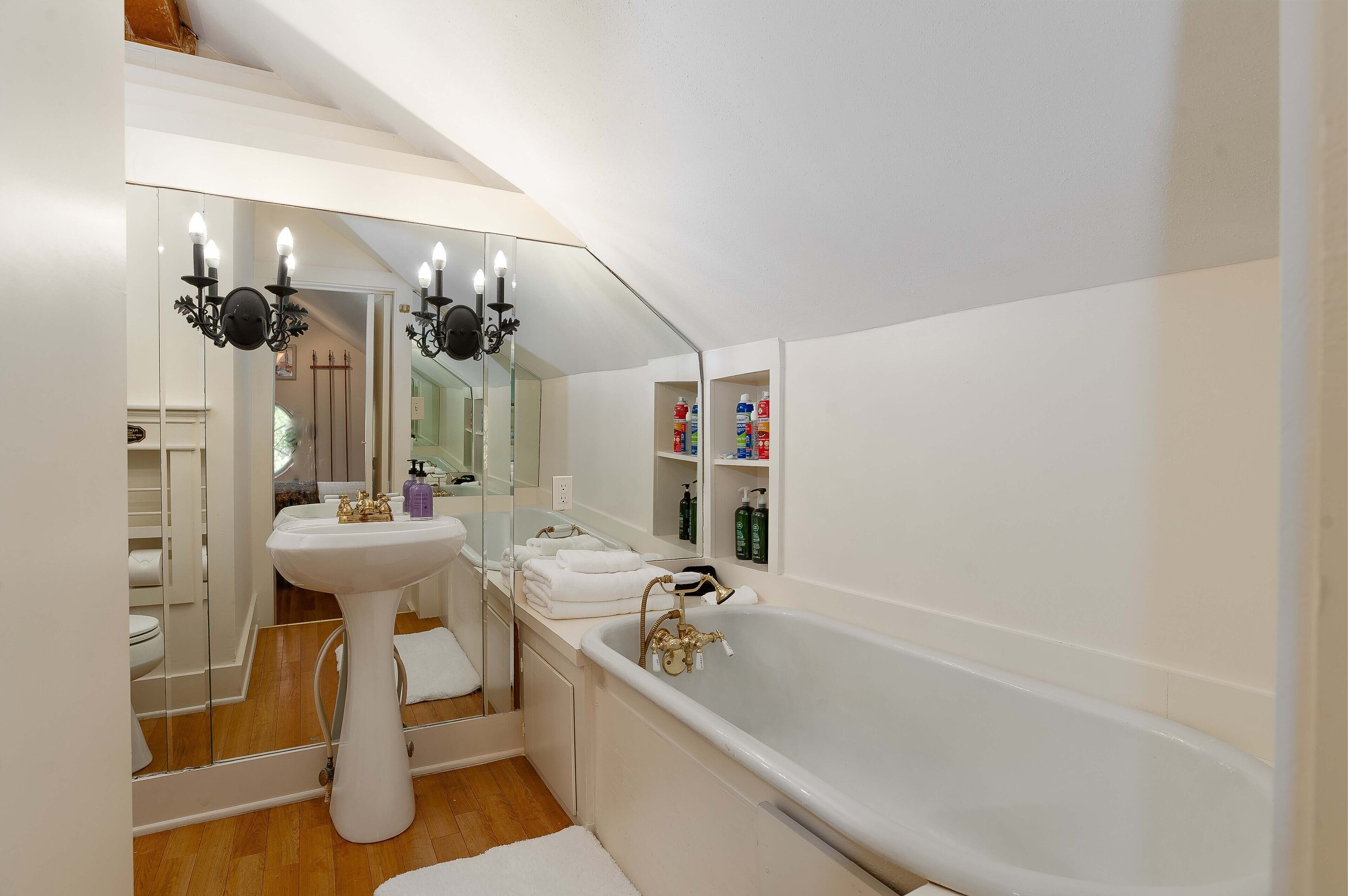 Un baño moderno con un lavamanos pedestal, una bañera independiente y un espejo grande.