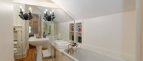 Un baño moderno con un lavamanos pedestal, una bañera independiente y un espejo grande.