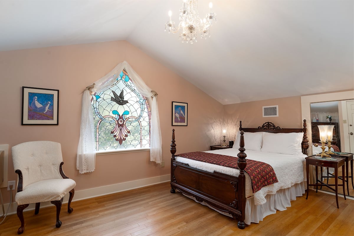 Une chambre à coucher avec un lit à baldaquin en bois, une chaise blanche, un vitrail et un lustre.