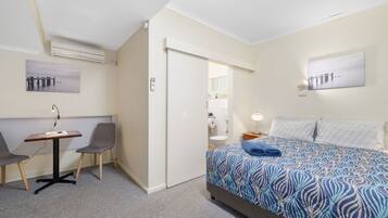 A hotel room with a bed, a desk with two chairs, a door, and a wall-mounted air conditioner.