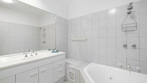 A modern bathroom with a large mirror, two sinks, a bathtub, and a shower. - Navigators Motel (Port Lincoln)