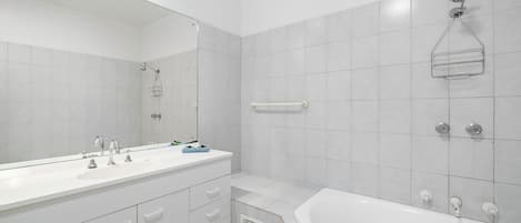 A modern bathroom with a large mirror, two sinks, a bathtub, and a shower.