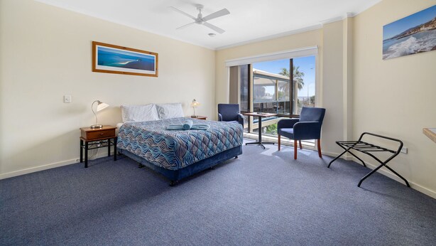 A hotel room with a bed, a desk, a chair, a ceiling fan, and a large window with a view. - Navigators Motel (Port Lincoln)