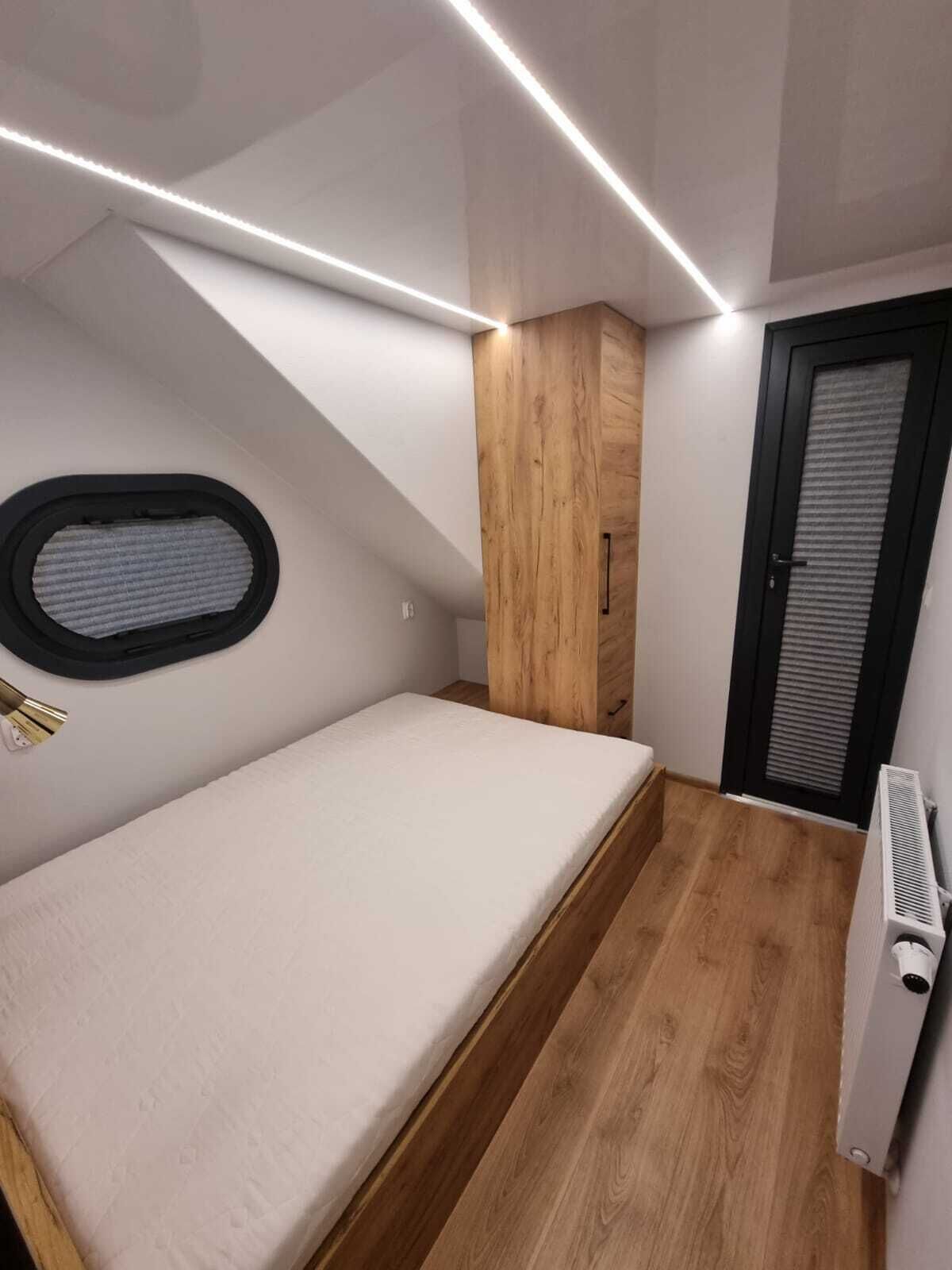 Ein kleines Schlafzimmer mit einem Bett, einem Holzschrank, einem Heizkörper und einem Fenster mit Jalousien.