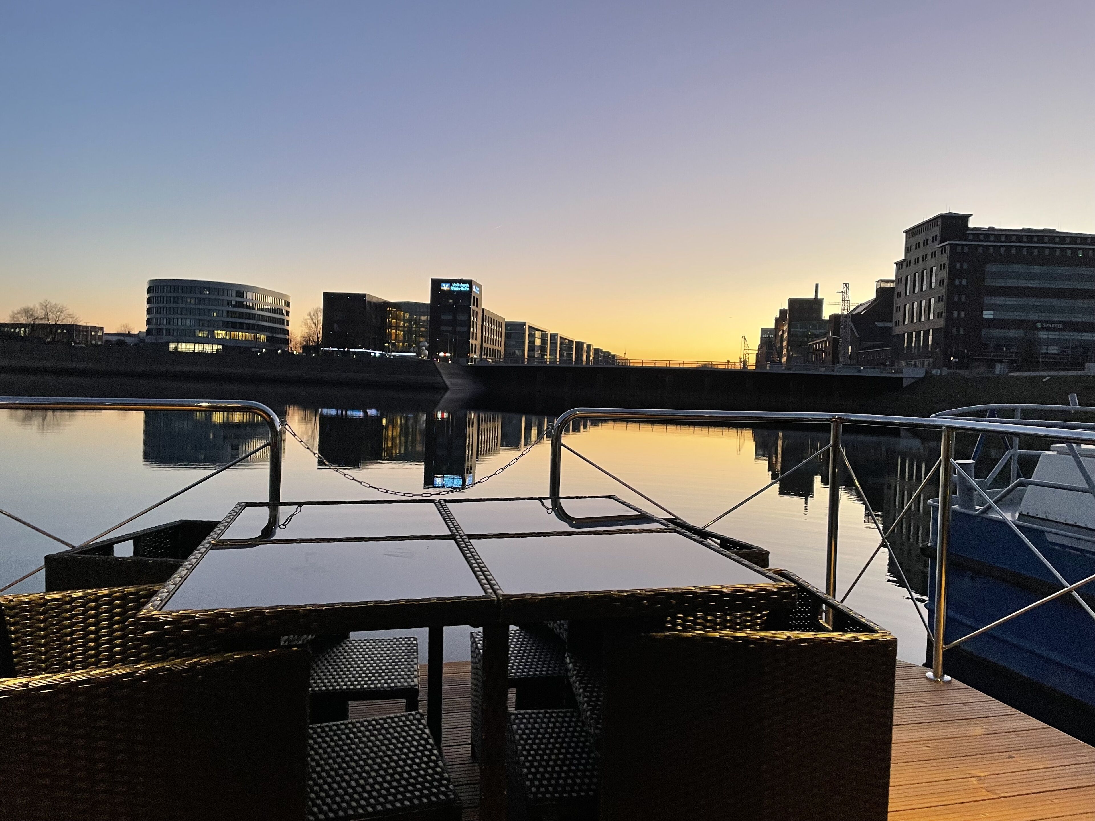 A waterfront deck with a view of the city skyline reflected in the water.