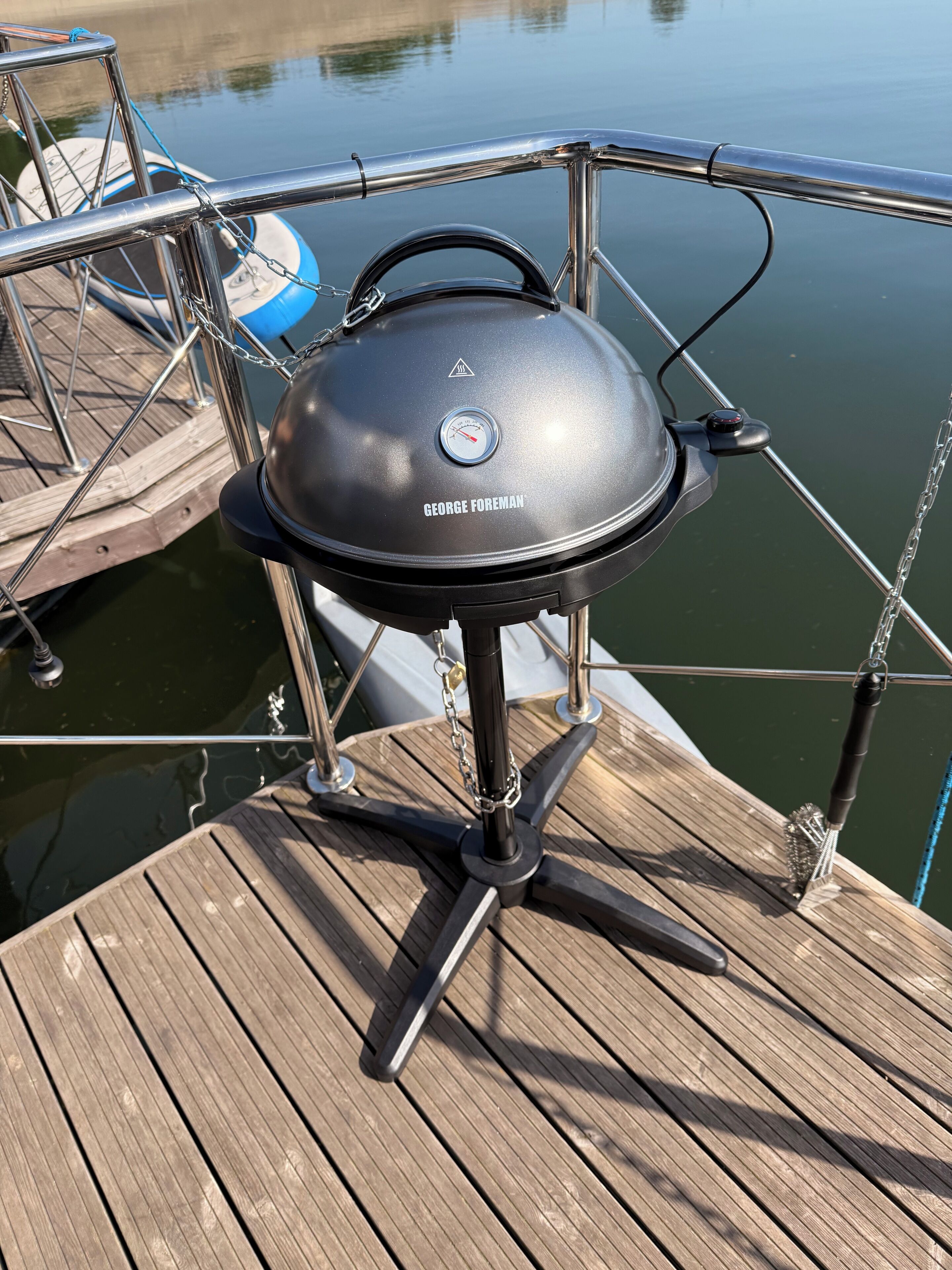 A George Foreman grill on a wooden dock with a body of water in the background.