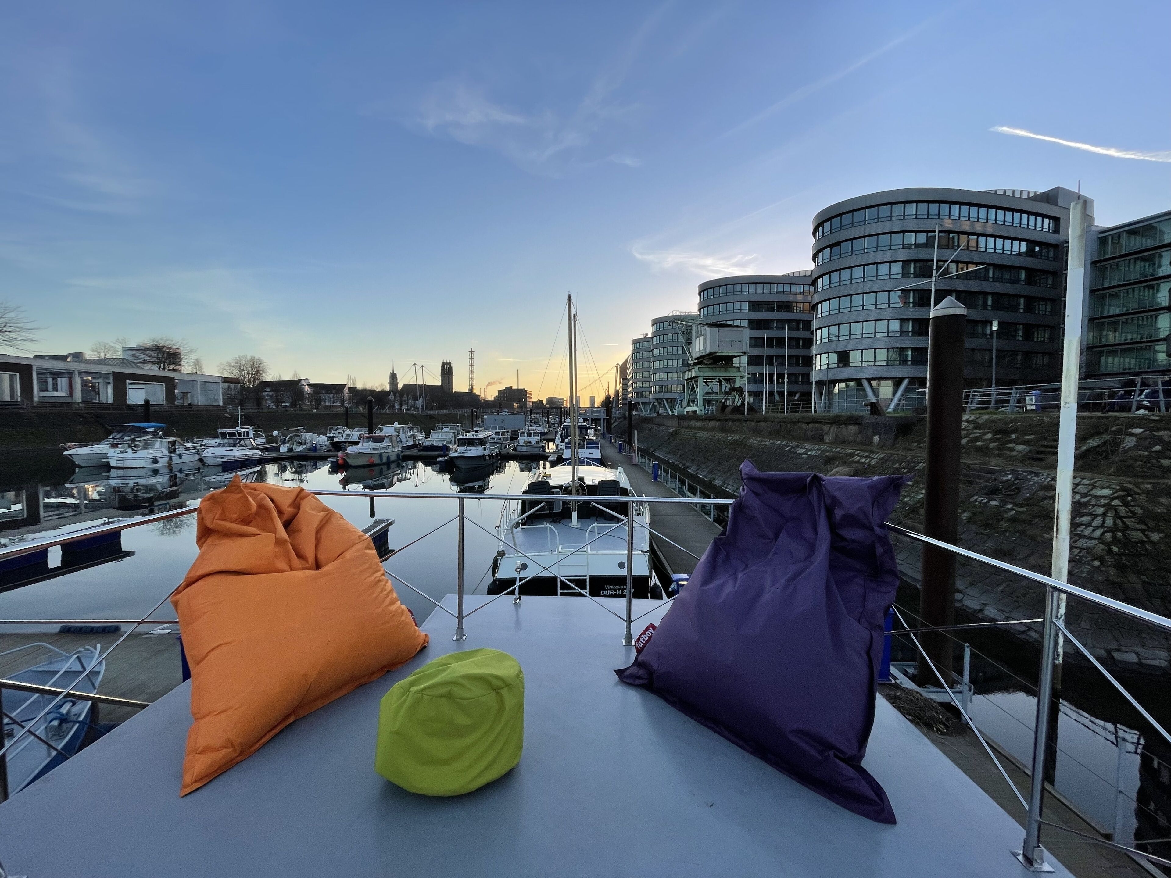 A view from a balcony overlooking a marina with boats, a modern building, and a clear sky.