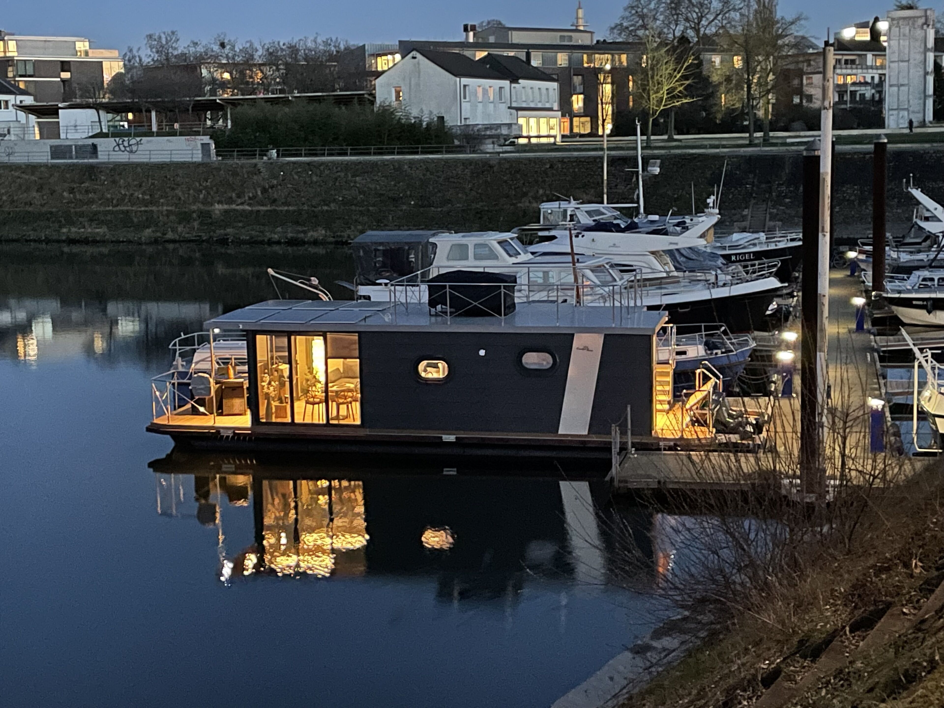 A houseboat docked at a marina with a covered deck area and a small outdoor seating space.