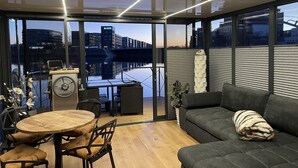 A modern interior with a dining area, a sofa, and a view of a cityscape through large windows. - Hausboot Lore (Duisburg)