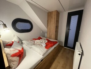 A compact bedroom with a bed, a small window, a wooden wardrobe, and a door. - Hausboot Lore (Duisburg)