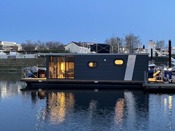 A houseboat docked at a marina with a large window and a small deck area. - Hausboot Lore (Duisburg)