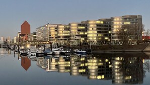 A waterfront building complex with multiple floors and a marina with boats. - Hausboot Lore (Duisburg)