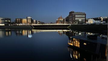 A waterfront view with buildings reflecting on calm water, a dock with a boat, and a bridge in the background.