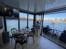 Un comedor moderno con vista a un río, un barco a lo lejos y un espacio con paredes de vidrio.