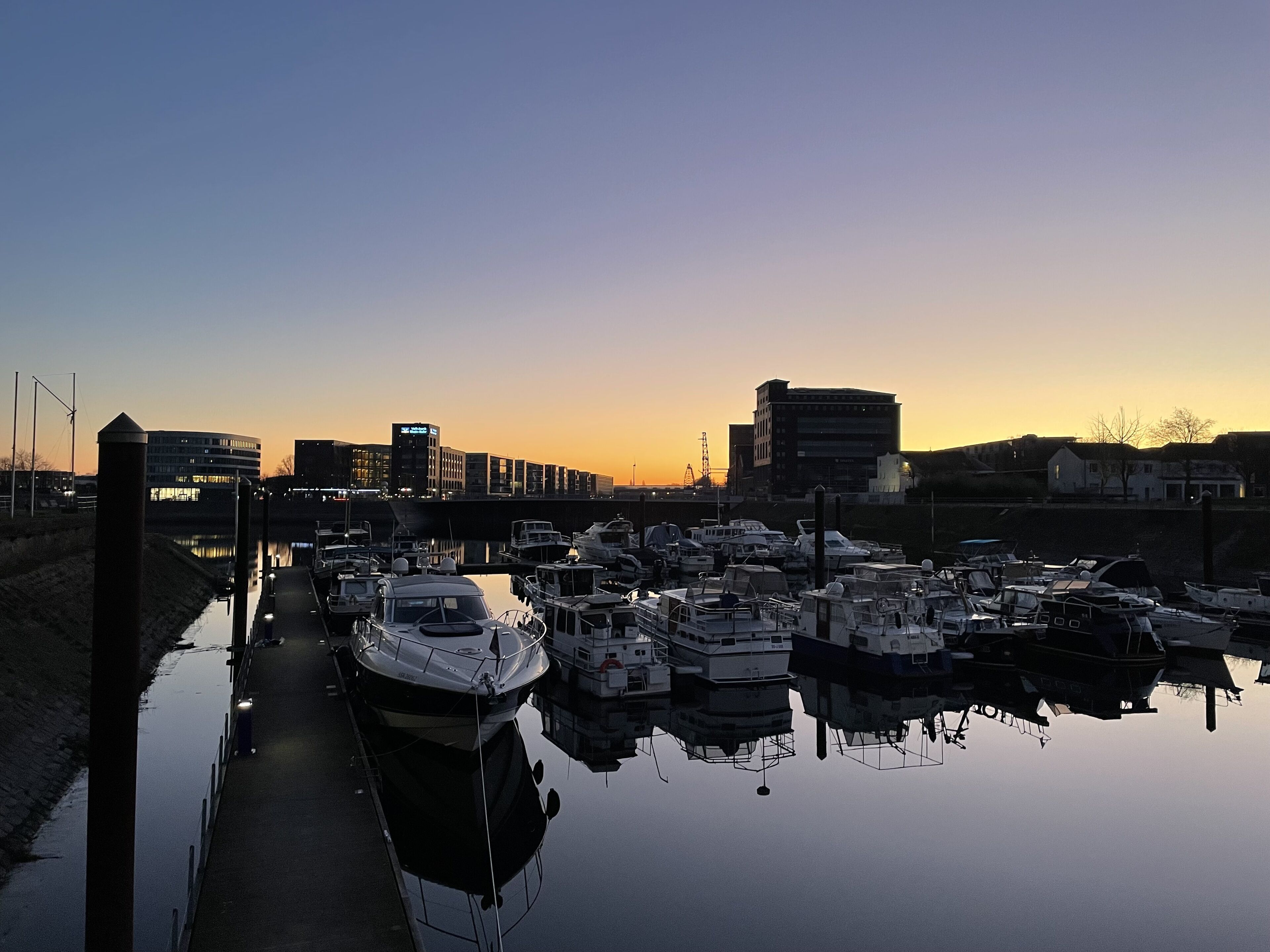 Een jachthaven met stilgelegde boten, een waterweg en gebouwen op de achtergrond.