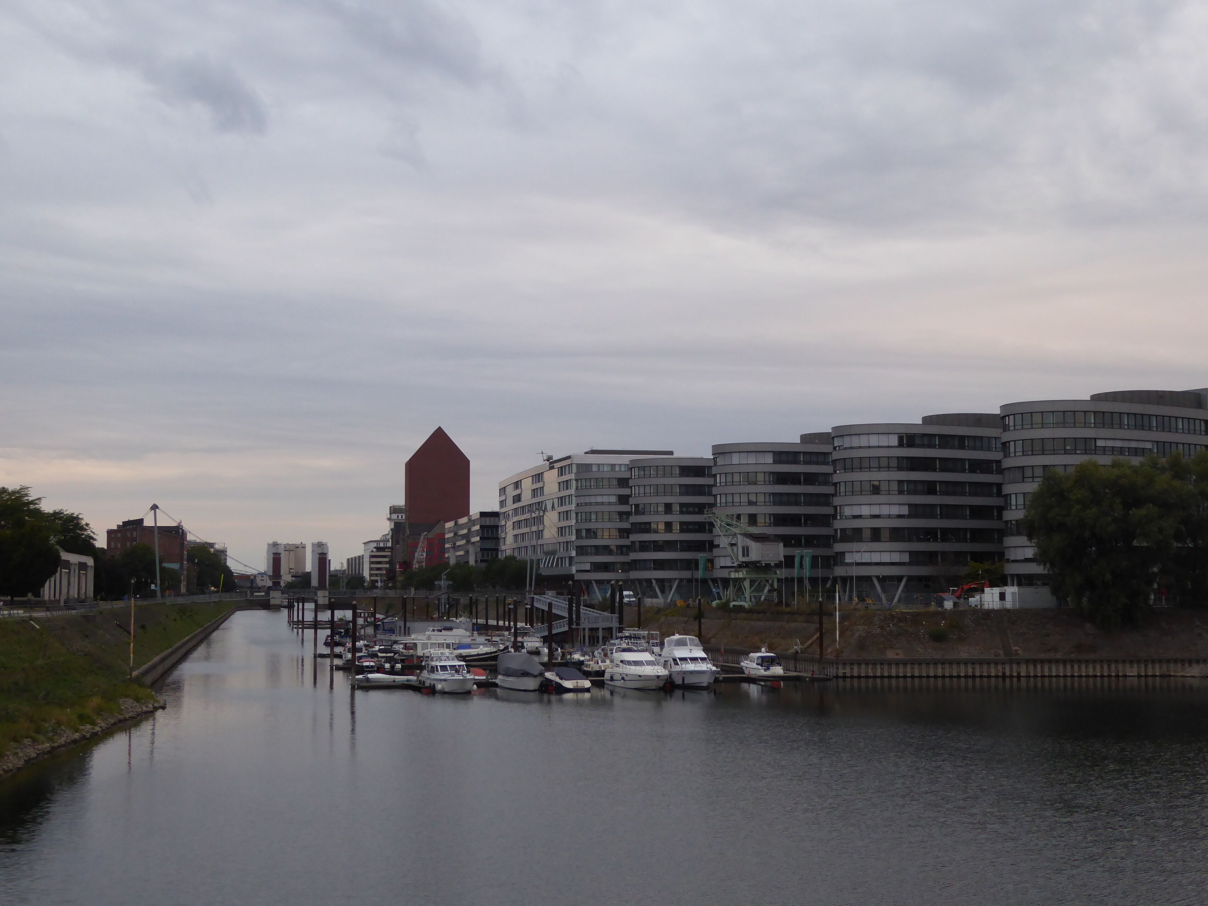A marina with several boats docked, surrounded by modern buildings and a canal.