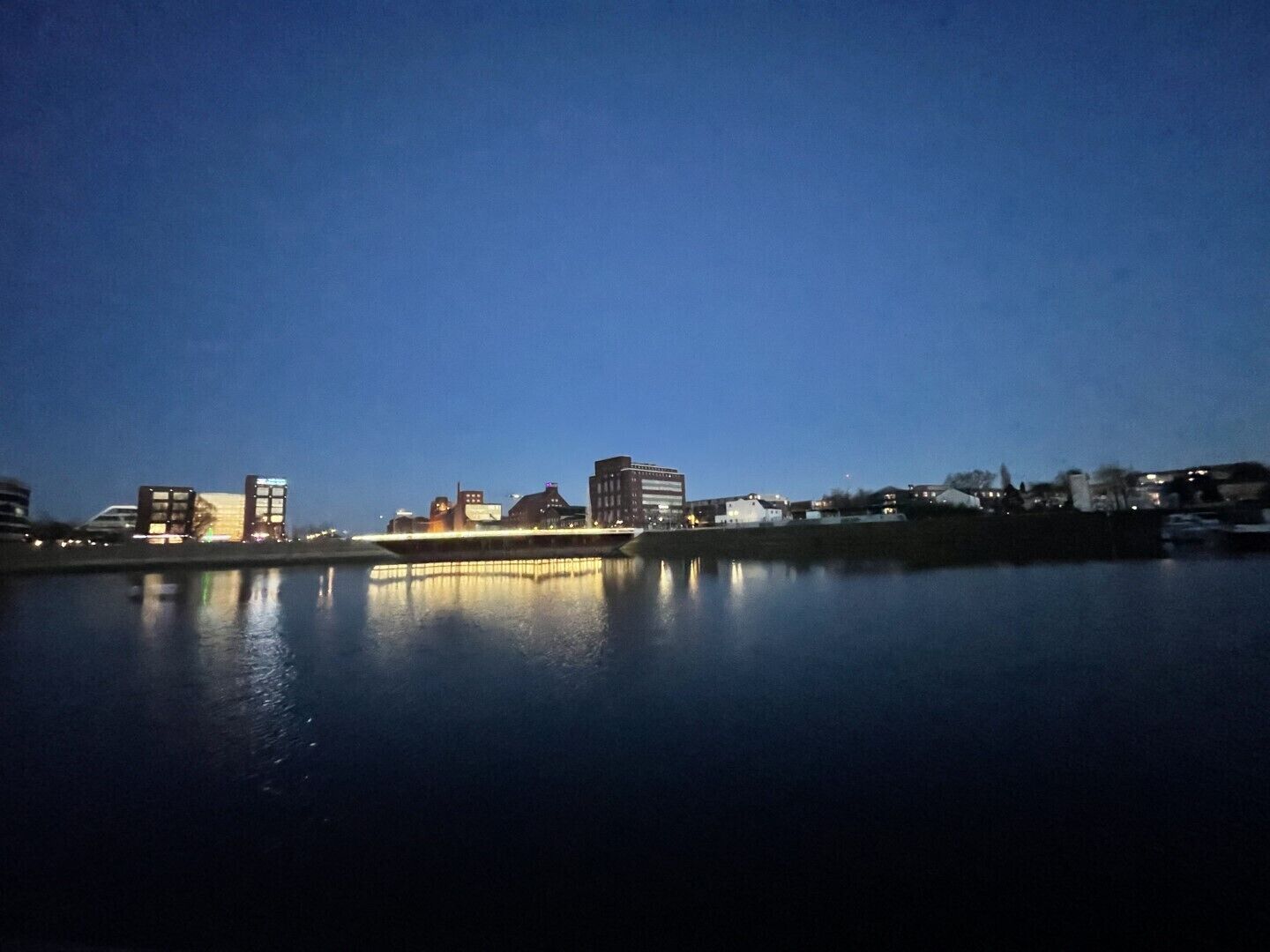 Kaupungin siluetti auringonlaskun aikaan, rakennukset heijastuvat tyynestä vedestä.