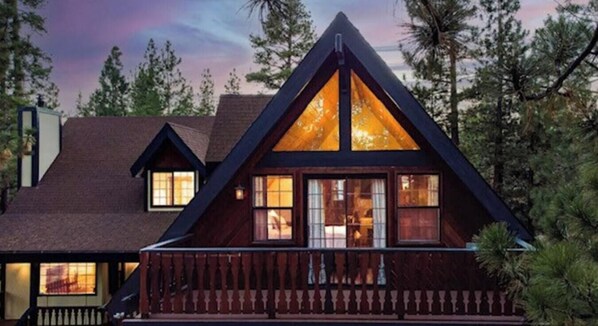 Une cabane dotée d’un toit triangulaire, de grandes fenêtres et d’une terrasse en bois.