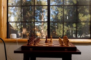 Un jeu d’échecs est posé sur une table devant une fenêtre, d’où l’on aperçoit des arbres.