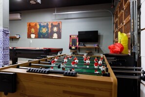 A foosball table in a room with a pool table, a television, and a bear-themed painting on the wall. - 🐻FamilyCabin🍿TheaterRoom🎱GameRoom🔋EVCharger 🐶PetFriendly (Big Bear)