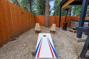 A backyard with a shuffleboard table, two wooden chairs, a wooden fence, and a barbecue grill. - 🐻FamilyCabin🍿TheaterRoom🎱GameRoom🔋EVCharger 🐶PetFriendly (Big Bear)