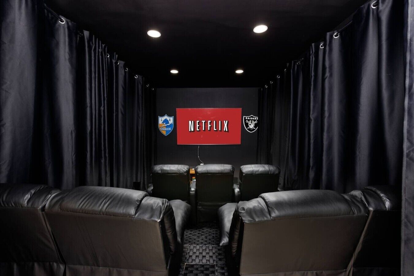 Et mørkt rum med læderstole, et Netflix-skilt og to holdlogoer på væggen.