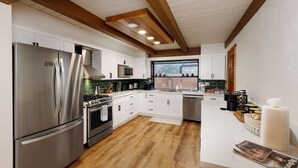 Una cocina moderna con electrodomésticos de acero inoxidable, armarios blancos y techo de madera.
