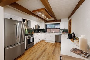 Una cocina moderna con electrodomésticos de acero inoxidable, armarios blancos y techo de madera.