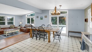 A spacious living room with a large dining table, a sofa, and a fireplace. There are multiple windows providing natural light and views of the outdoors. - Cardinals Perch (Campton)