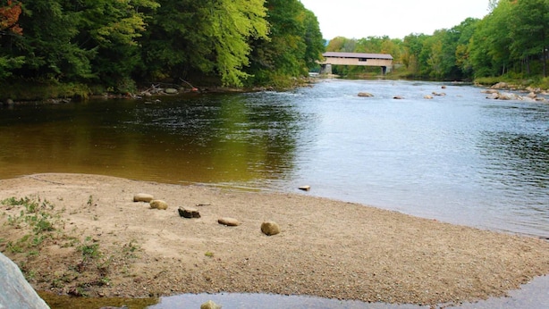 A river with a wooden bridge and a sandy bank with rocks. - Cardinals Perch (Campton)