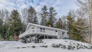 A two-story cabin with a white exterior, a balcony, and a chimney. It is surrounded by snow-covered ground and trees. - Cardinals Perch (Campton)