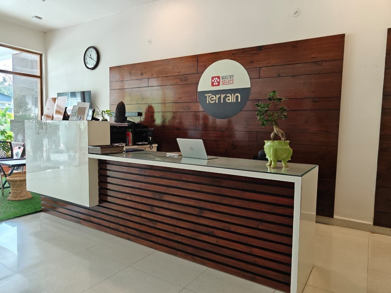A reception desk with a sign reading 'MASTIFF SELECT Terrain,' a clock, and a laptop on the counter.