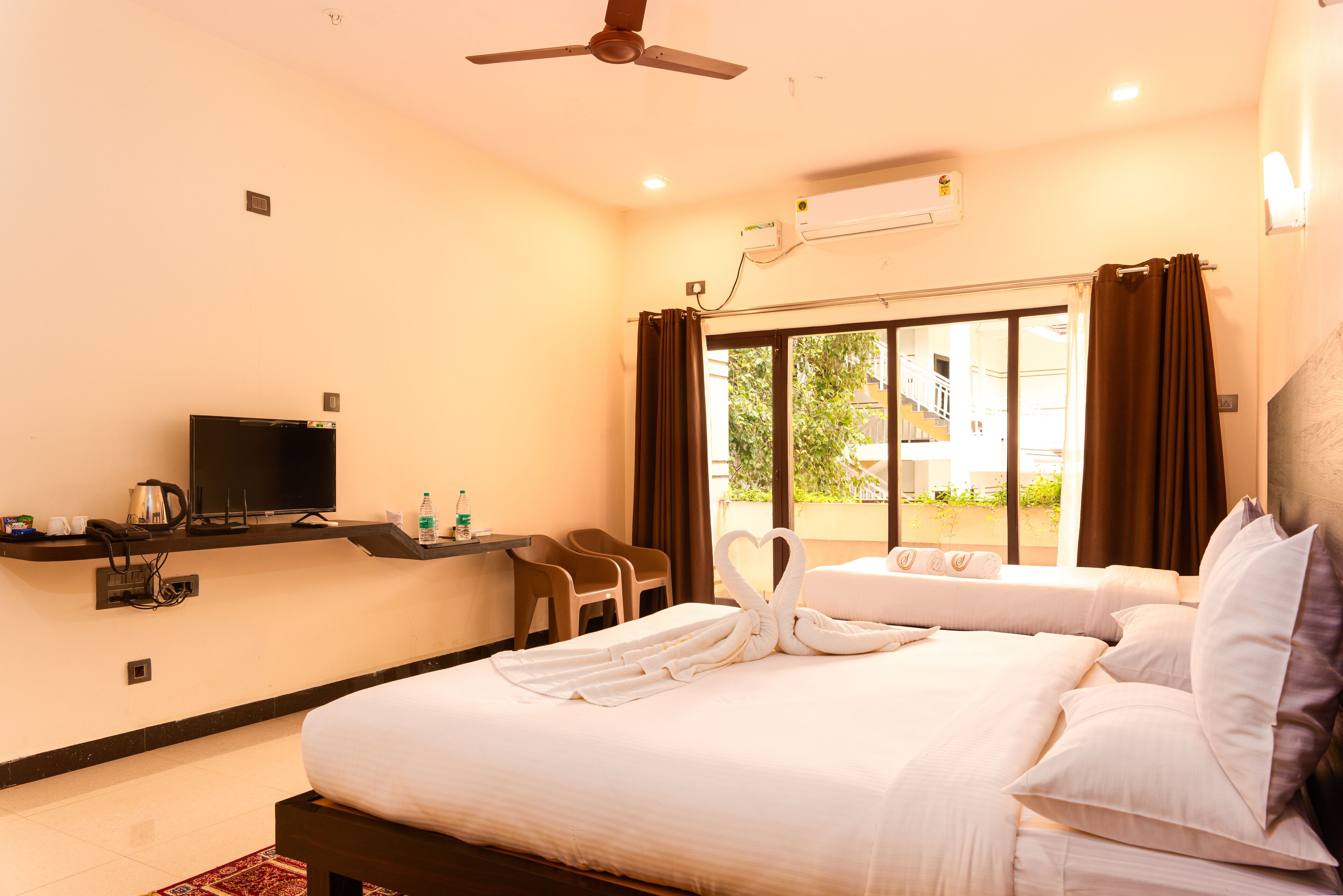 A hotel room with a bed, a television, a desk with a chair, and a window with curtains.