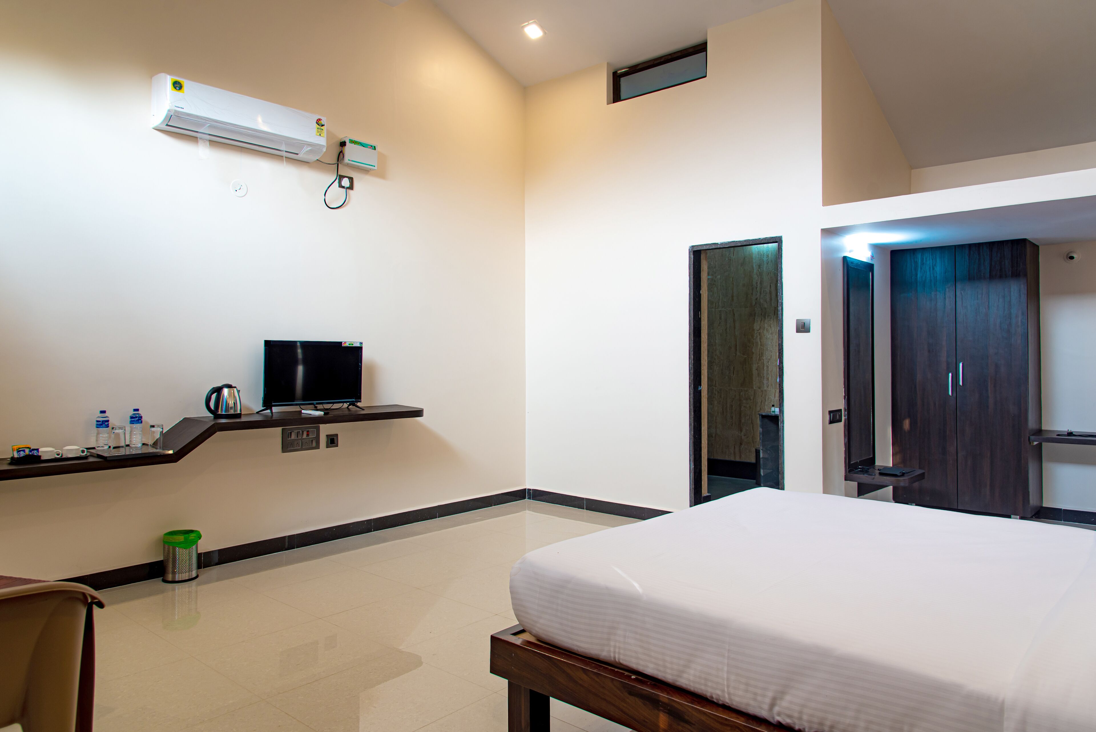A hotel room with a bed, a desk with a computer, a TV, and a minibar.