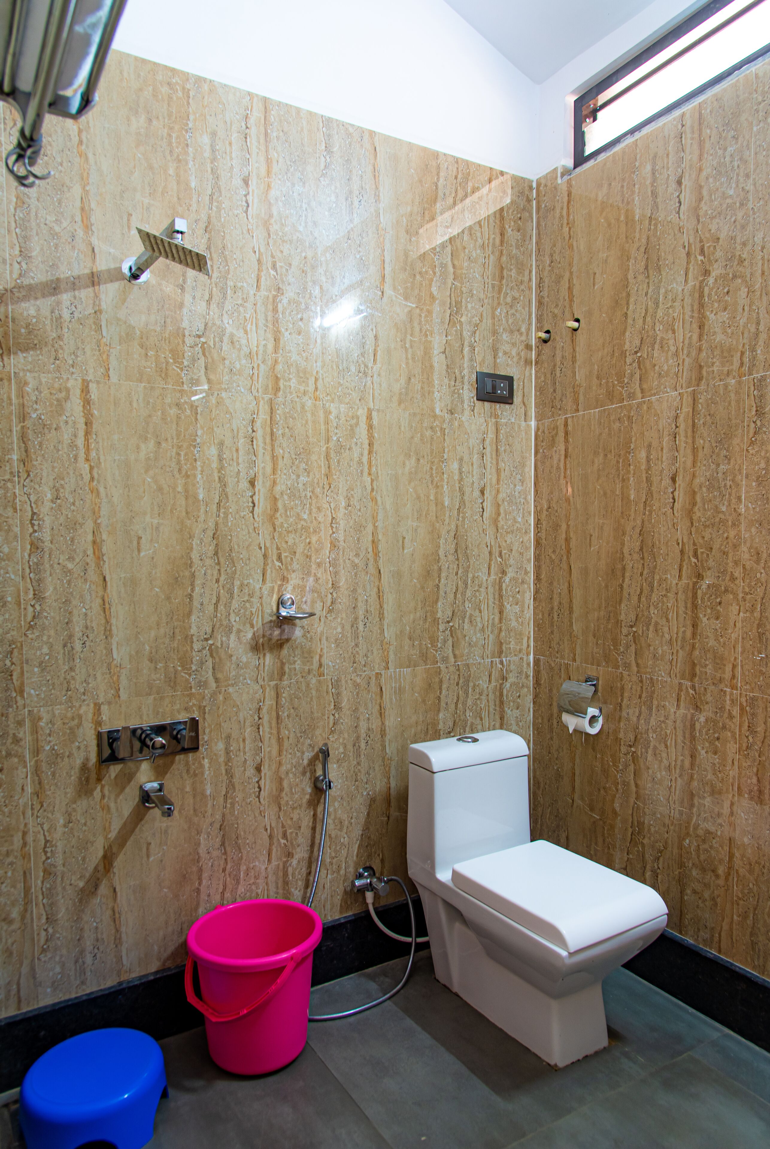 A bathroom with a toilet, a shower, and a pink bucket.