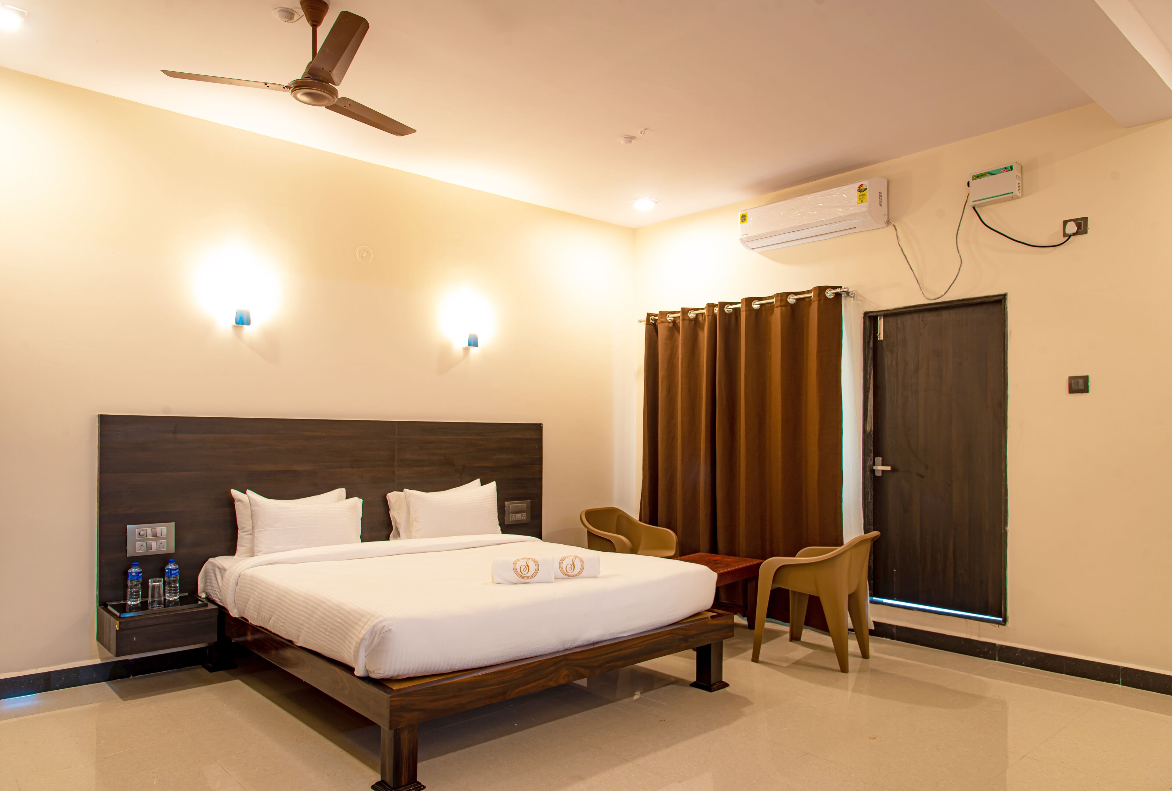 Ein Hotelzimmer mit Bett, Nachttisch, zwei Stühlen, Deckenventilator und Klimaanlage.