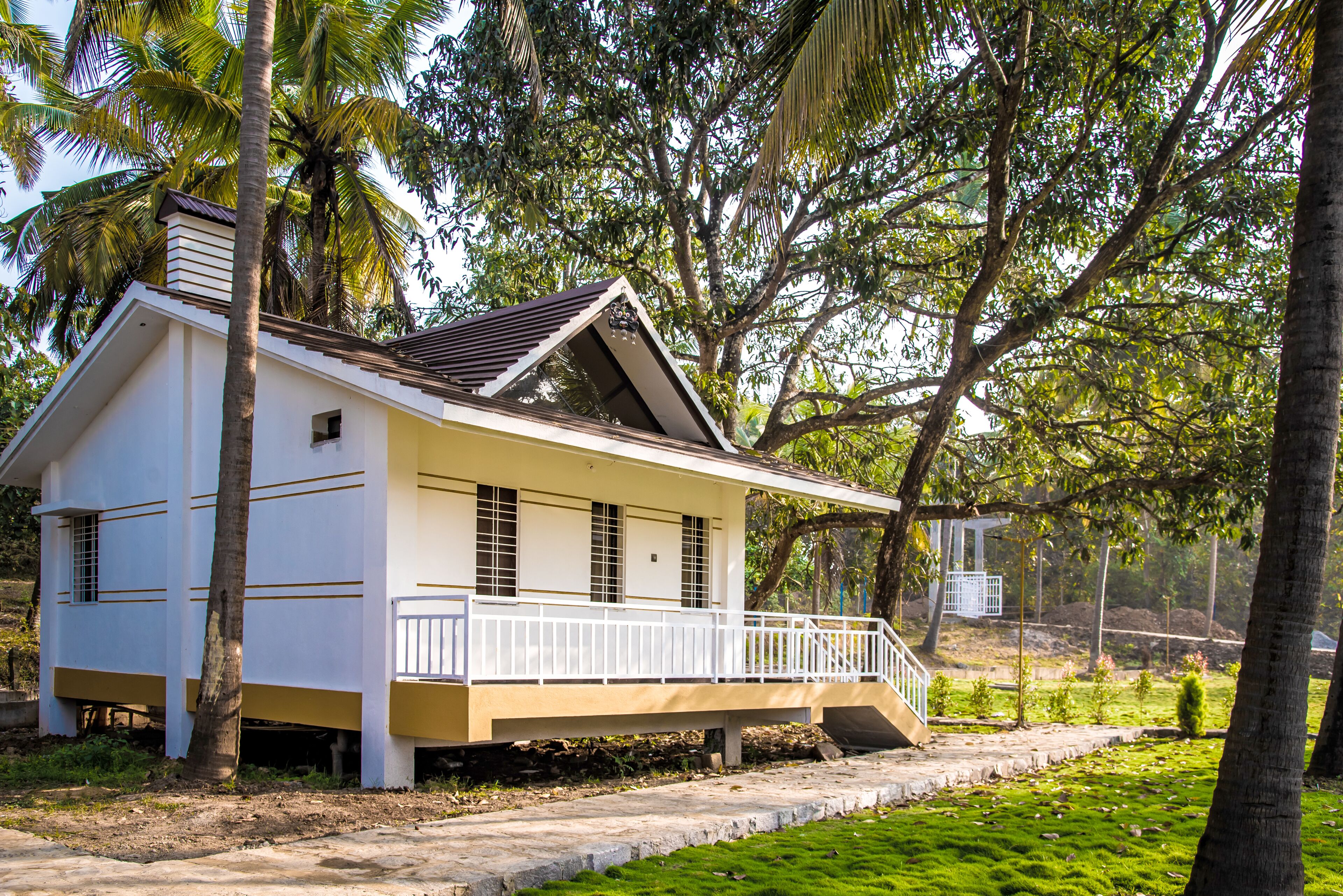 A single-story building with a white exterior and a brown roof, surrounded by lush greenery and palm trees.