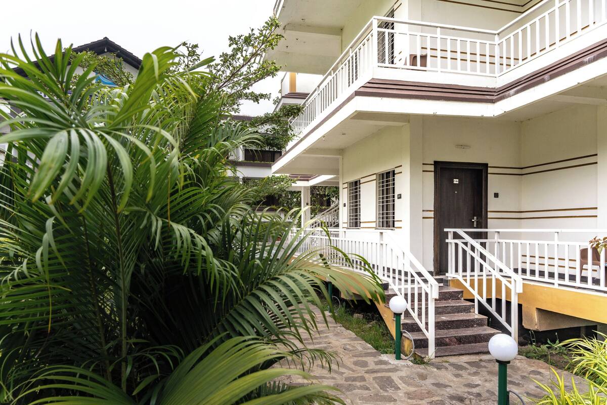 A multi-story building with a white exterior, a balcony on the upper floor, and a staircase leading to the entrance.