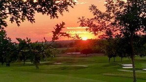 Un campo de golf al atardecer con un carrito de golf en primer plano.