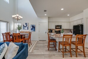 A spacious kitchen with white cabinets, a black refrigerator, and a dining area with wooden chairs and a blue sofa.