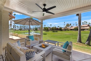 A covered outdoor seating area with a fire pit, patio furniture, and a view of a golf course. - Golf, Sun and Serenity: Your Relaxing Desert Escape Awaits! (Palm Desert)