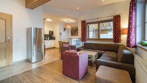 Een moderne woonkamer met een houten plafond, een keuken op de achtergrond en een groot raam met gordijnen.