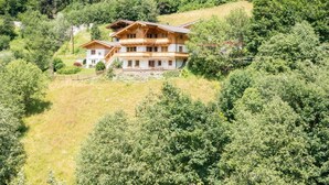 Een ruime, meerlaagse chalet met houten gevel, omgeven door dicht bos en heuvels.